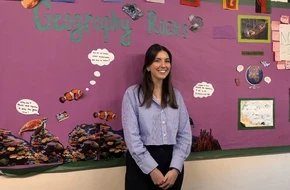 Hetta standing in front of a colourful ‘Geography Rocks’ classroom display.