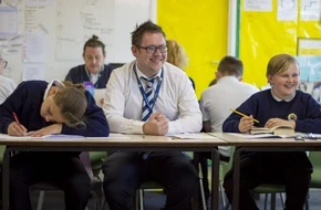 Teacher sitting at table in classroom with students