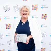 Julie Deville, OBE, holding a Pearson National Teaching Award at the award ceremony backdrop.