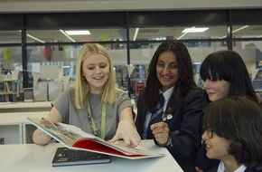 Teacher and students smile as they read a book together