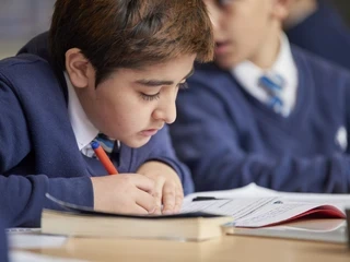 Student writing in book in class near classmate